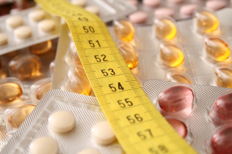 Measuring tape over weight loss pills on a table.