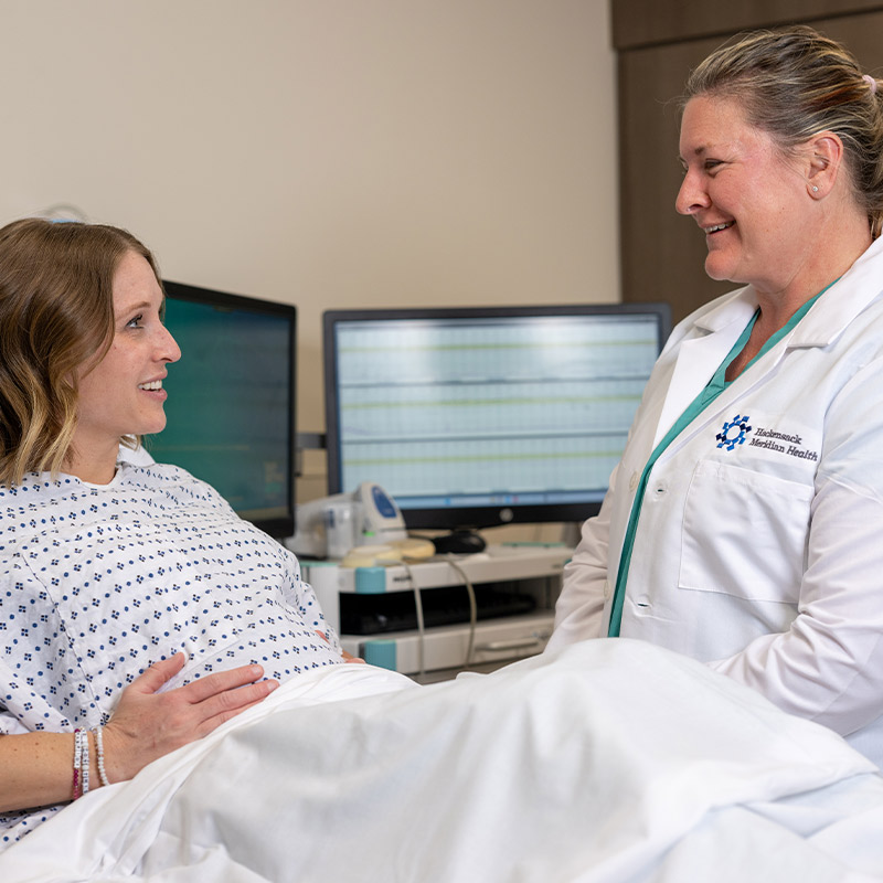 Pregnant patient in hospital gown sitting and talking with her OBGYN provider