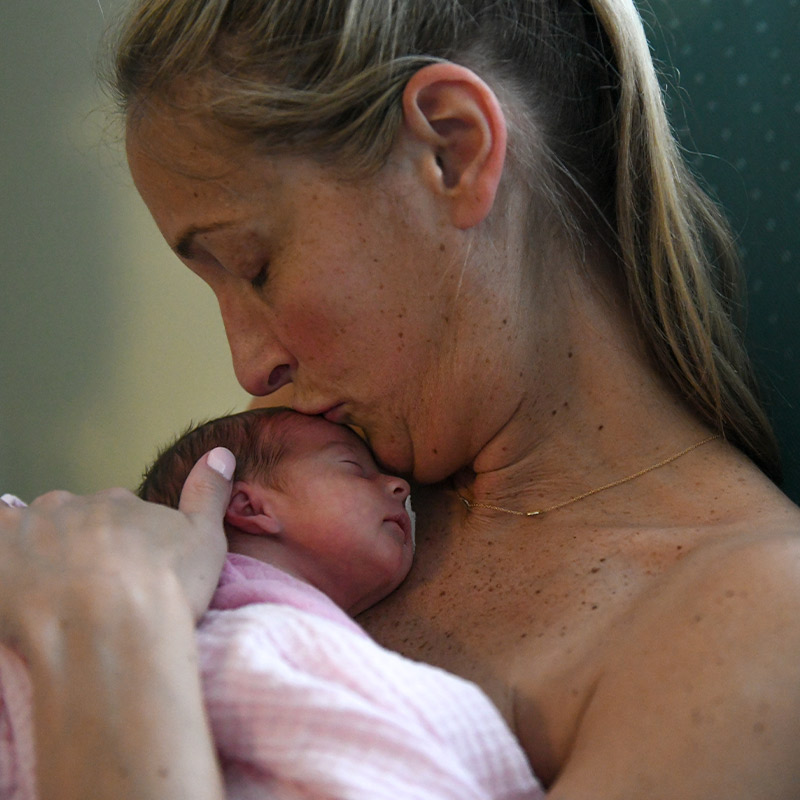 A mother holding and giving a kiss to her newborn who's wrapped in a pink blanket