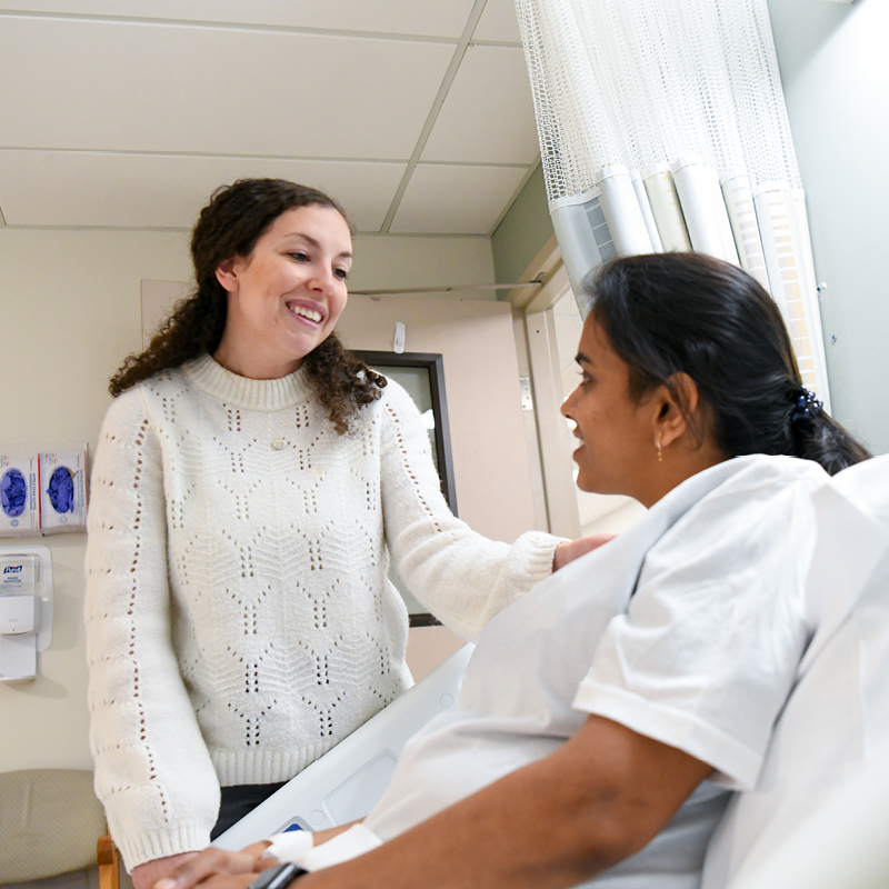 Woman speaking with a patient in a hospital room.
