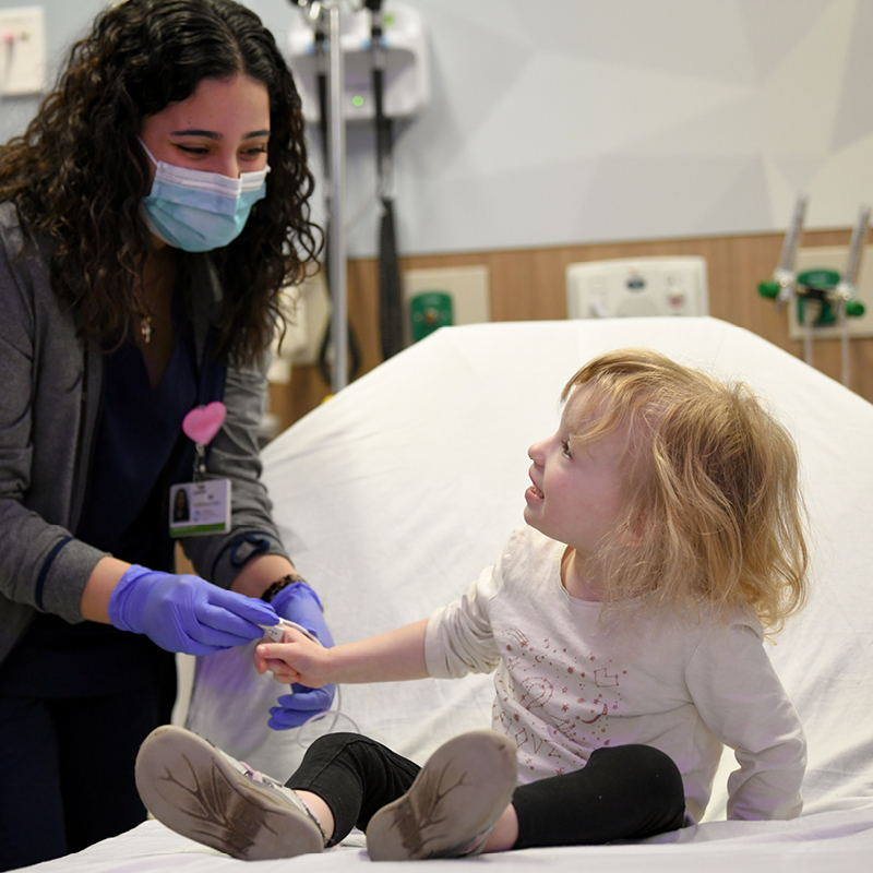 Healthcare worker holding a young patient's hand in a hospital room.