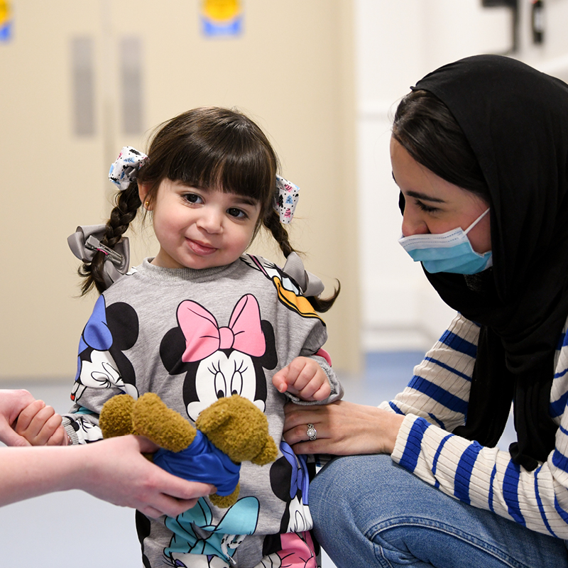 Young child holding a stuffed toy with a caregiver.