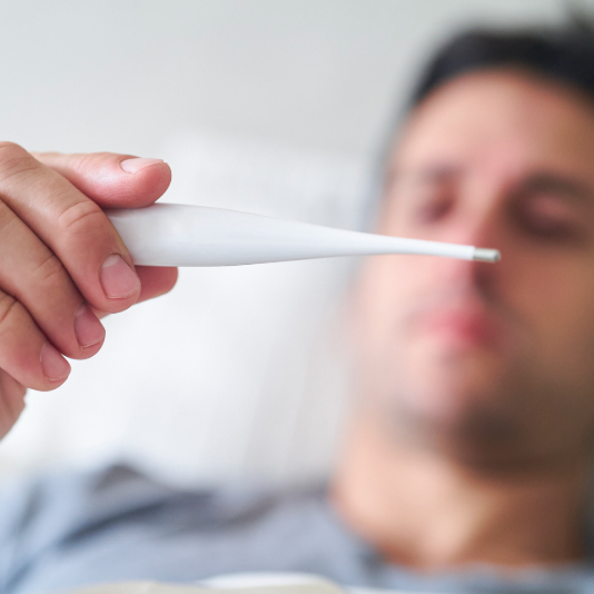 Close up shot of a man holding out a thermometer, taking his temperature while in bed.