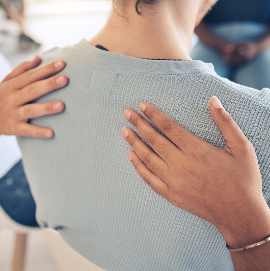 Hands on a woman's back, offering comfort in a support group setting.