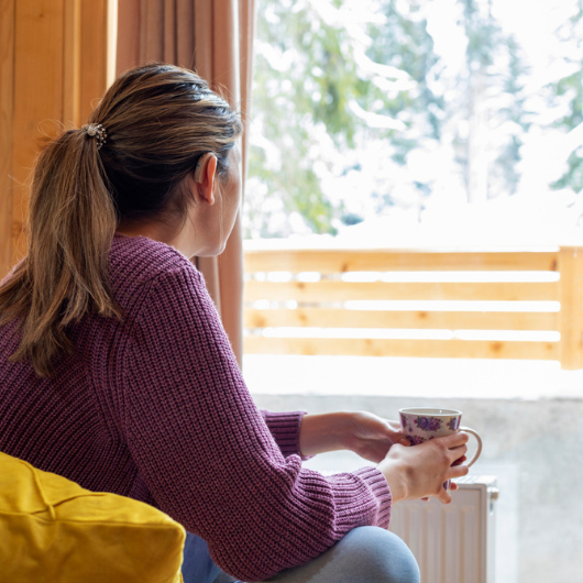  Beautiful young woman with hearing aid drinking tea and enjoying a winter view.