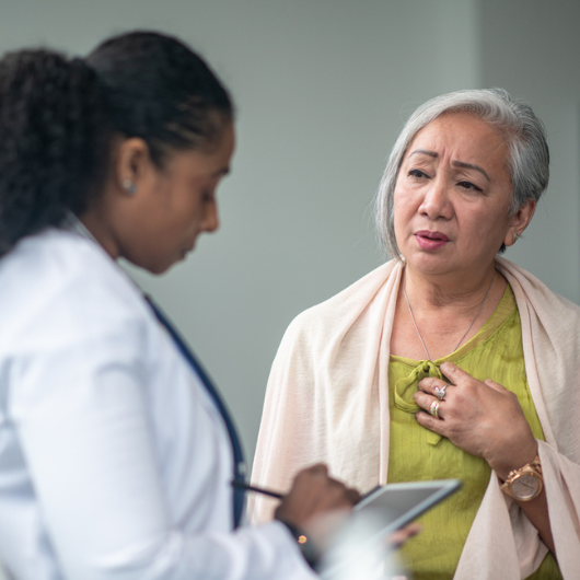 A senior woman shares her chest pain symptoms with her doctor at an appointment.
