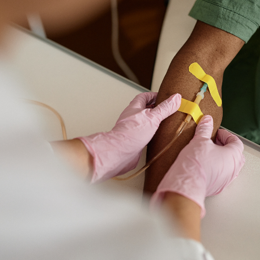 Close up view of a patient's arm receiving chemotherapy treatment with a nurse's hands assisting in care.