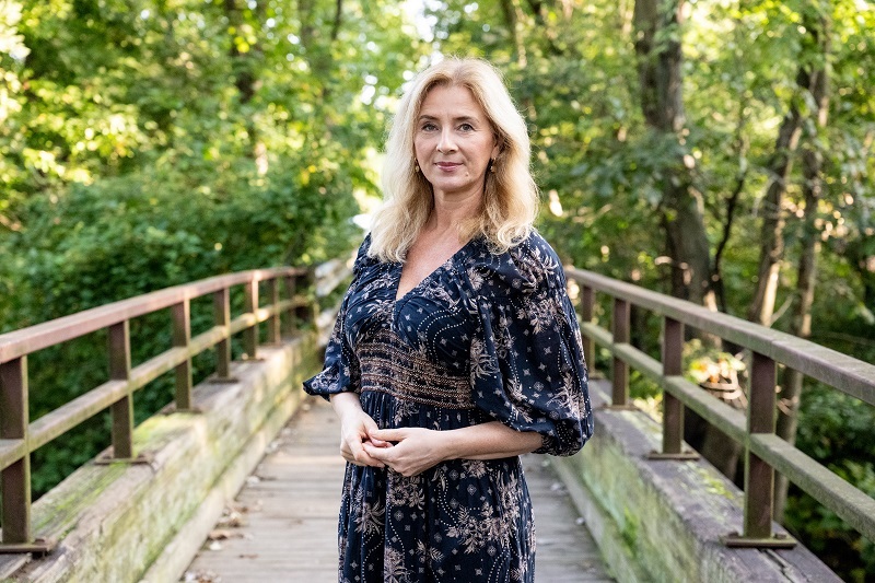 Jarmila Mallick standing on a bridge in the woods, smiling.