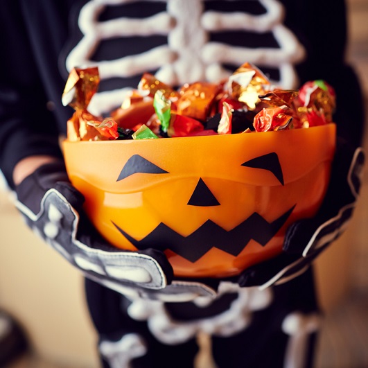 kid in skeleton costume holding bowl of halloween candy
