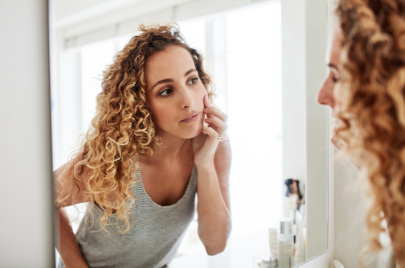 woman looking at skin in the mirror