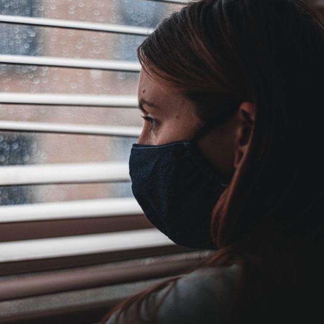 person wearing a mask looking out the window