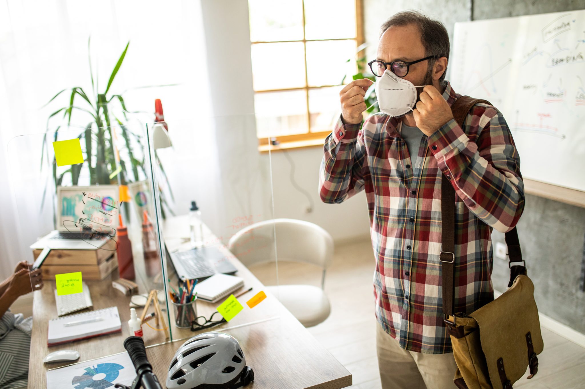 man standing by his desk putting a mask on