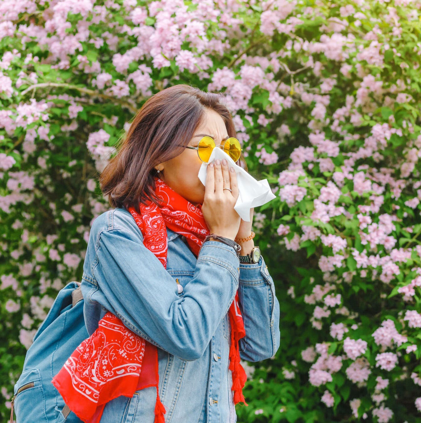 person with allergies blowing their nose outside