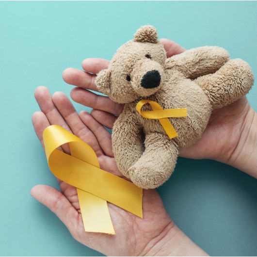 Hands holding children soft toy brown bear with yellow gold ribbon, Childhood cancer awareness