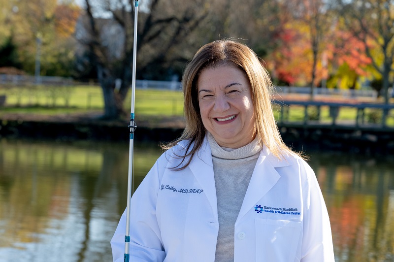 Neonatologist Charita Csiky, M.D. standing on a dock, smiling and holding a fishing pole.