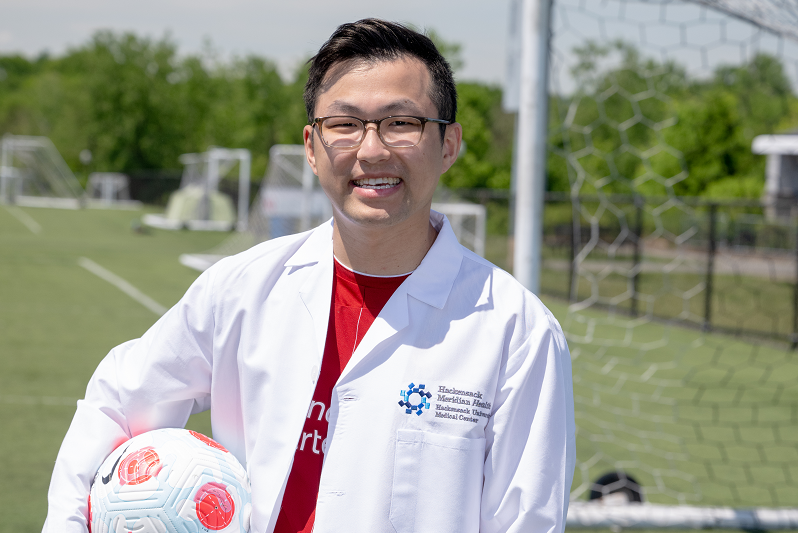 Dr. Alex Fu, standing in front of a soccer net, holding a soccer ball, smiling.