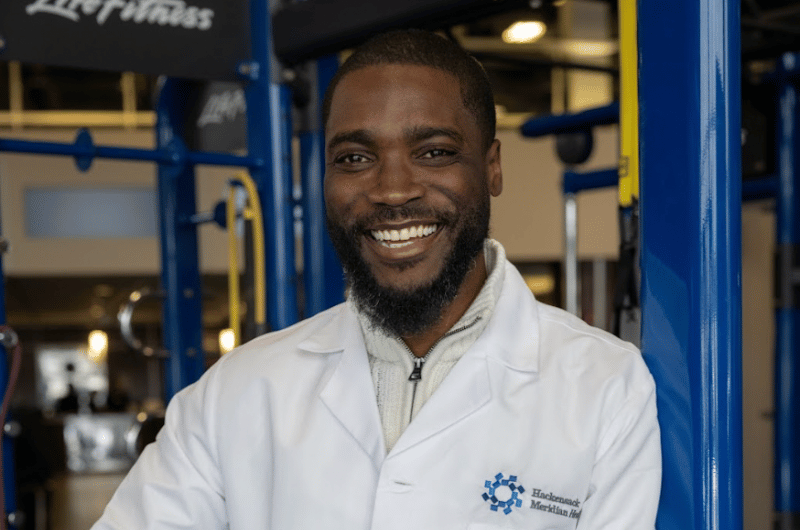 Primary care physician Lwoodsky Charles, M.D., leans against some exercise equipment in a gym.