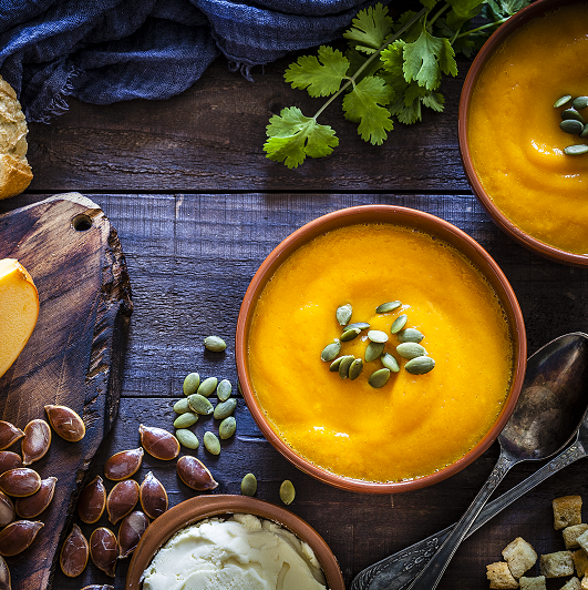 Assortment of pumpkin foods on a table - pumpkin soup, pumpkin seeds, and cut pumpkin.