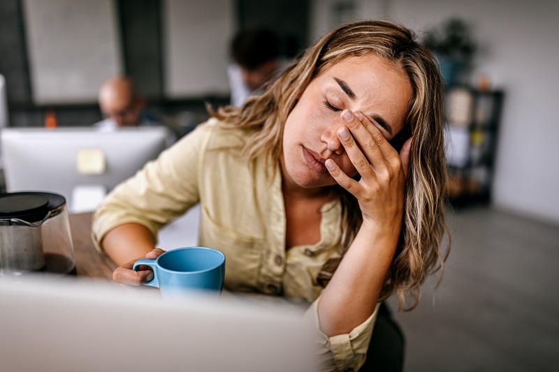 Young woman rubbing her eyes, suffering from a migraine while working from home