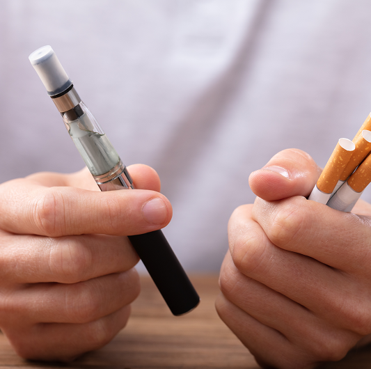 Man holding e-cigarette and cigarettes in his hands.
