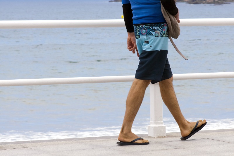 Man walking along the beach in flip flops.