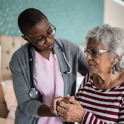 Home caregiver helping a senior woman with Parkinson's disease standing in the bedroom