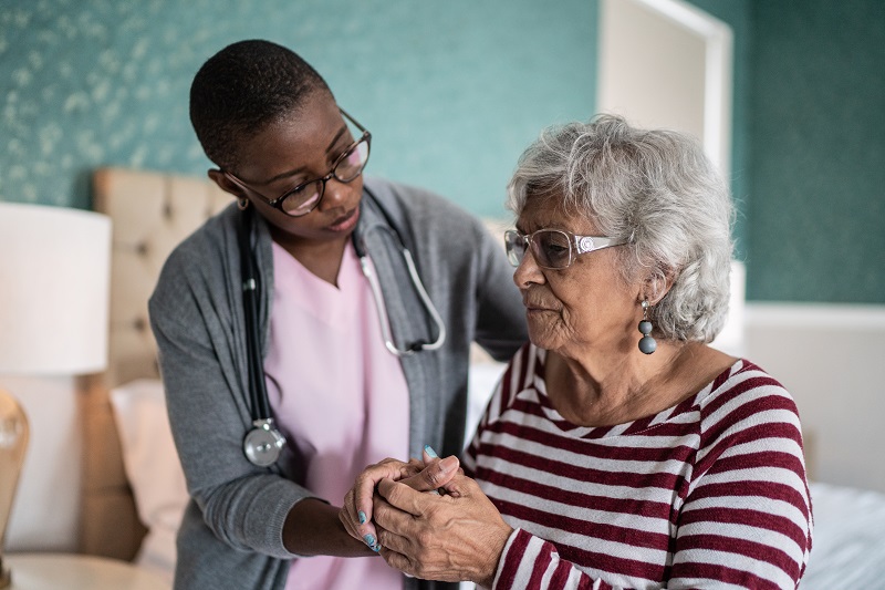 Home caregiver helping a senior woman with Parkinson's disease standing in the bedroom