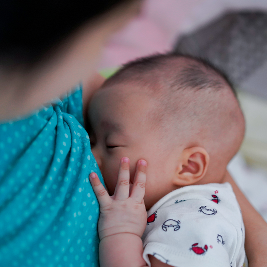 Mother breastfeeding and hugging baby. Baby holding her hand on face while eating milk before sleeping.
