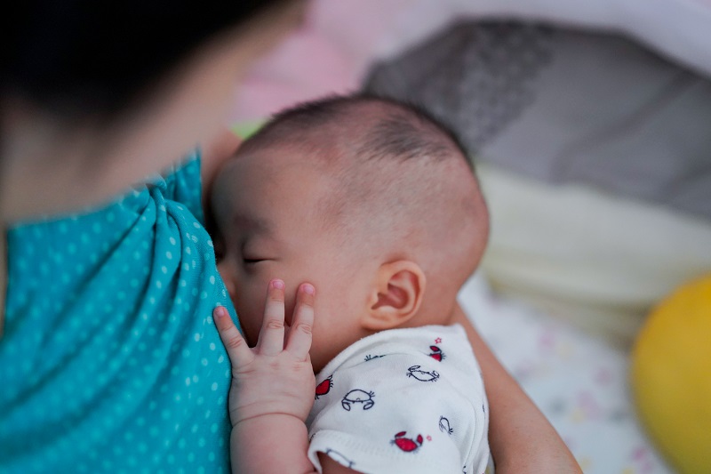 Mother breastfeeding and hugging baby. Baby holding her hand on face while eating milk before sleeping.