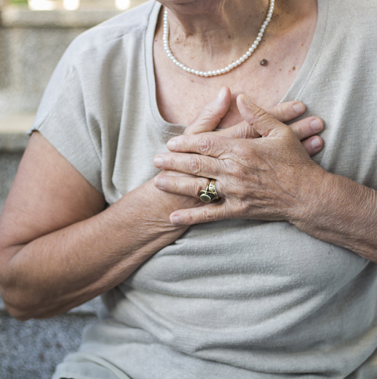 Close up of an elderly woman clutching her chest from chest pain. Heart disease concept. 