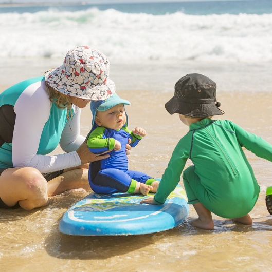 parent and kids playing on beach with sun protective clothes on