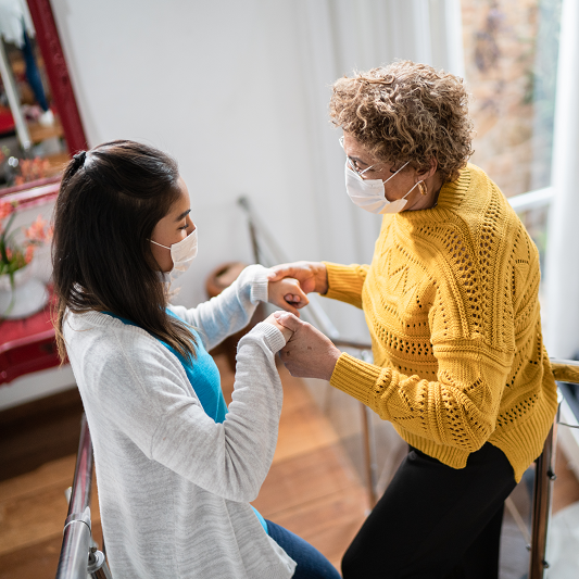 Young woman helping an older woman walking down stairs, holding hands. Older woman is suffering from Parkinson's disease.