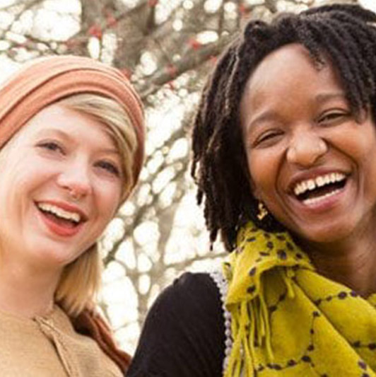 Two women smiling outside on a sunny day.