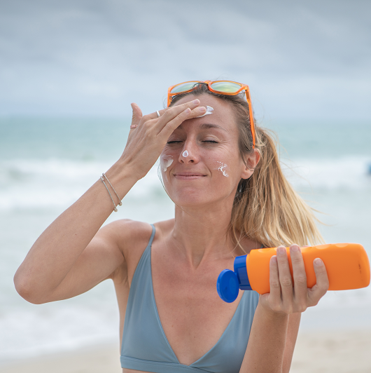 Young woman on beach applying sunscreen on her face, protection on skin and sunbathing tan concept