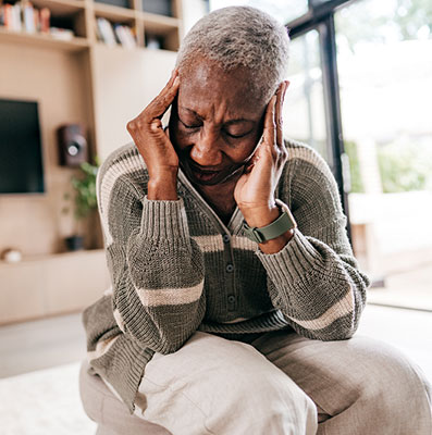 Older woman grasps the sides of her head due to a headache. 