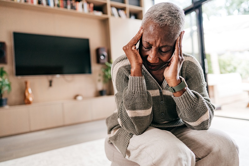 Older woman grasps the sides of her head due to a headache. 