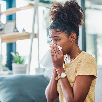 Woman blowing her nose on the couch not feeling well - allergies or a cold