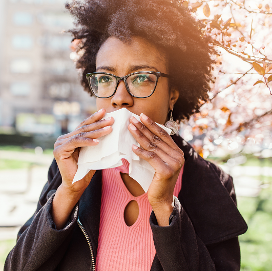 Woman blowing her nose in the park, feeling the affects of allergies