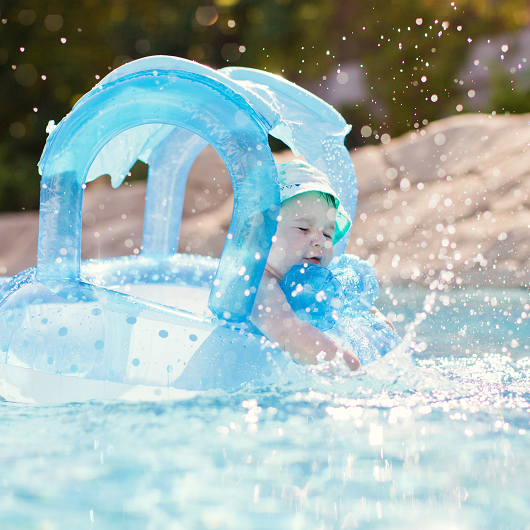 baby sitting in a floating device in a swimming pool splashing 