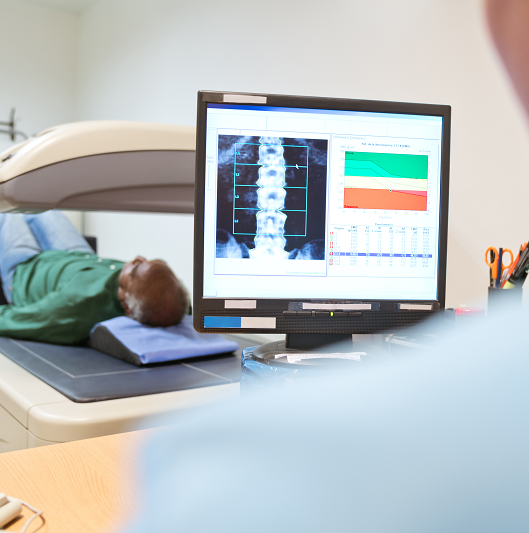 Healthcare worker analyzing x-ray image on computer monitor. Senior male patient is lying on examination table. 