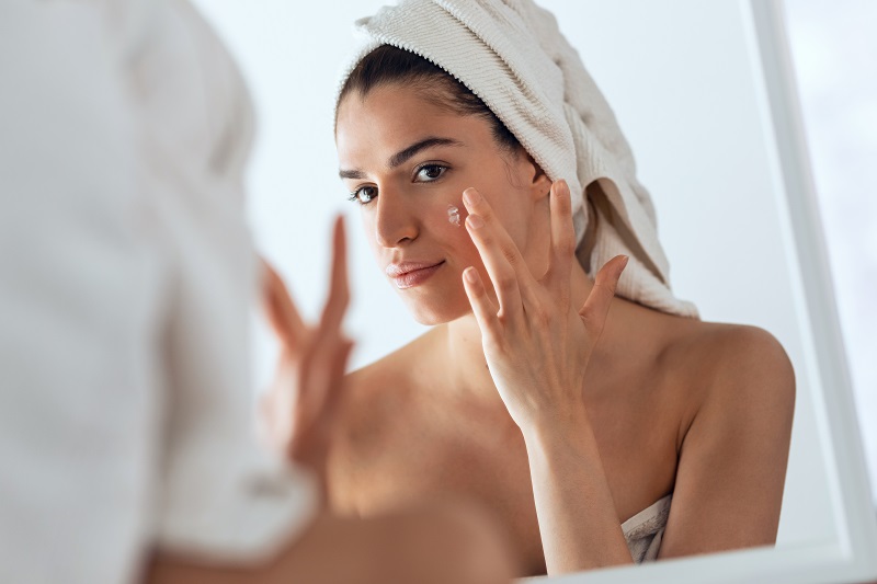 Young woman in the bathroom treating her acne with toothpaste. 