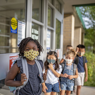 Children waiting in a line outside of their school with masks on. 