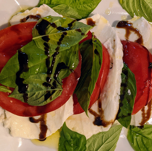 Caprese salad on a plate - tomatoes, mozzarella, and vinaigrette drizzle.