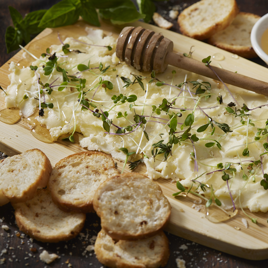 The Viral Butterboard with Fresh Herbs, Micro Greens, Organic Honey and Toasted Baguette Slices on a Bamboo Cutting Board