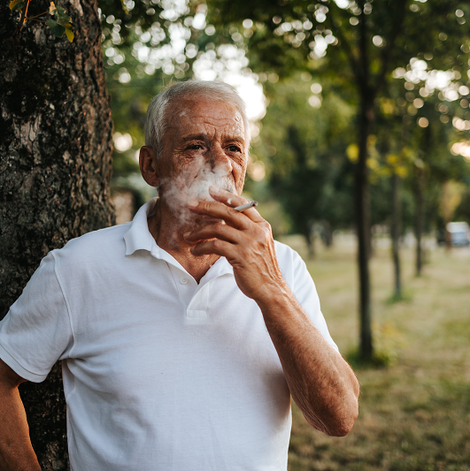 Older man smoking a cigarette outside.