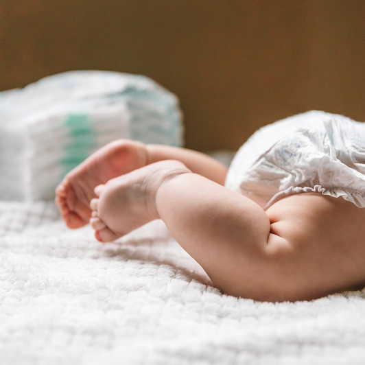 A baby's diaper and legs on a blanket with a pile of diapers in the background. What your baby's poop means.