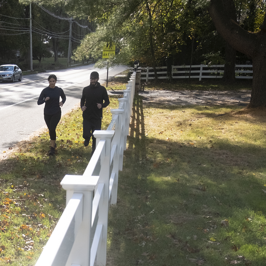 Woman and man running along the side of the road on soft grass.