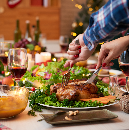 Woman's hands cutting thanksgiving dinner at a table full of food and drinks.