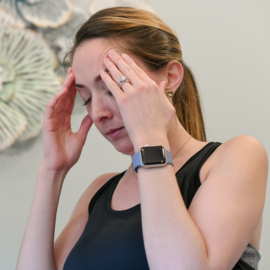 Woman with her hands on her forehead, clenching from a headache or migraine.
