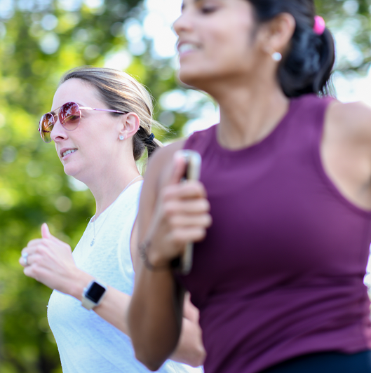 Close up of two young women jogging together outside.